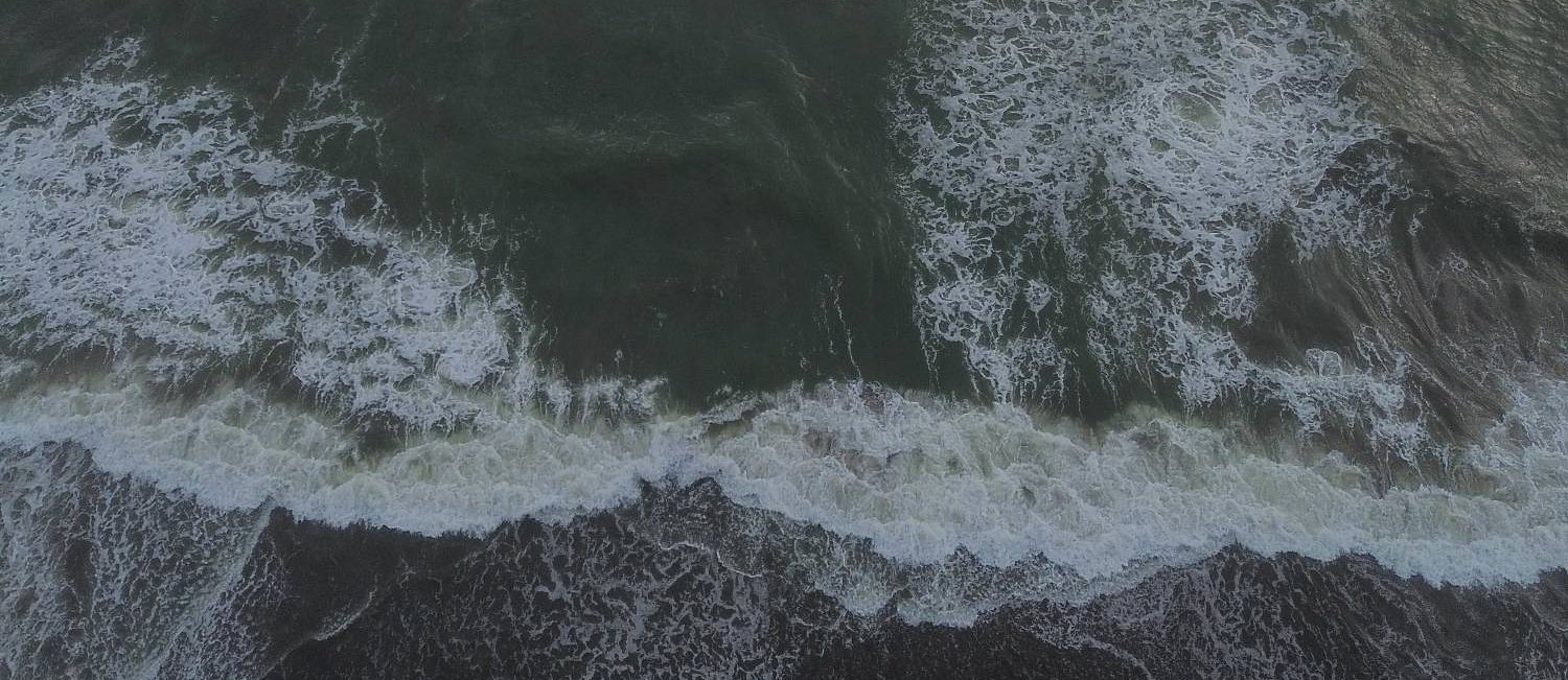 The surf at Kedungu seen from above, white water rolling onto the black sand